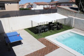 A backyard with a pool, a ping pong table, and outdoor seating under umbrellas.