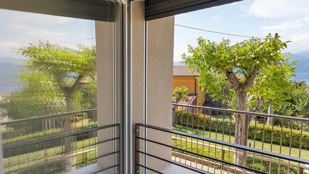 Un balcon avec une rambarde en métal, une vue sur un arbre et un bâtiment en arrière-plan.
