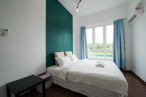 Hotellihuone, jossa on sänky, pieni pöytä, yöpöytä, ikkuna verhoilla ja ilmastointilaite.