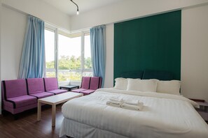A hotel room with a bed, a sofa, a table, and a view of greenery outside.
