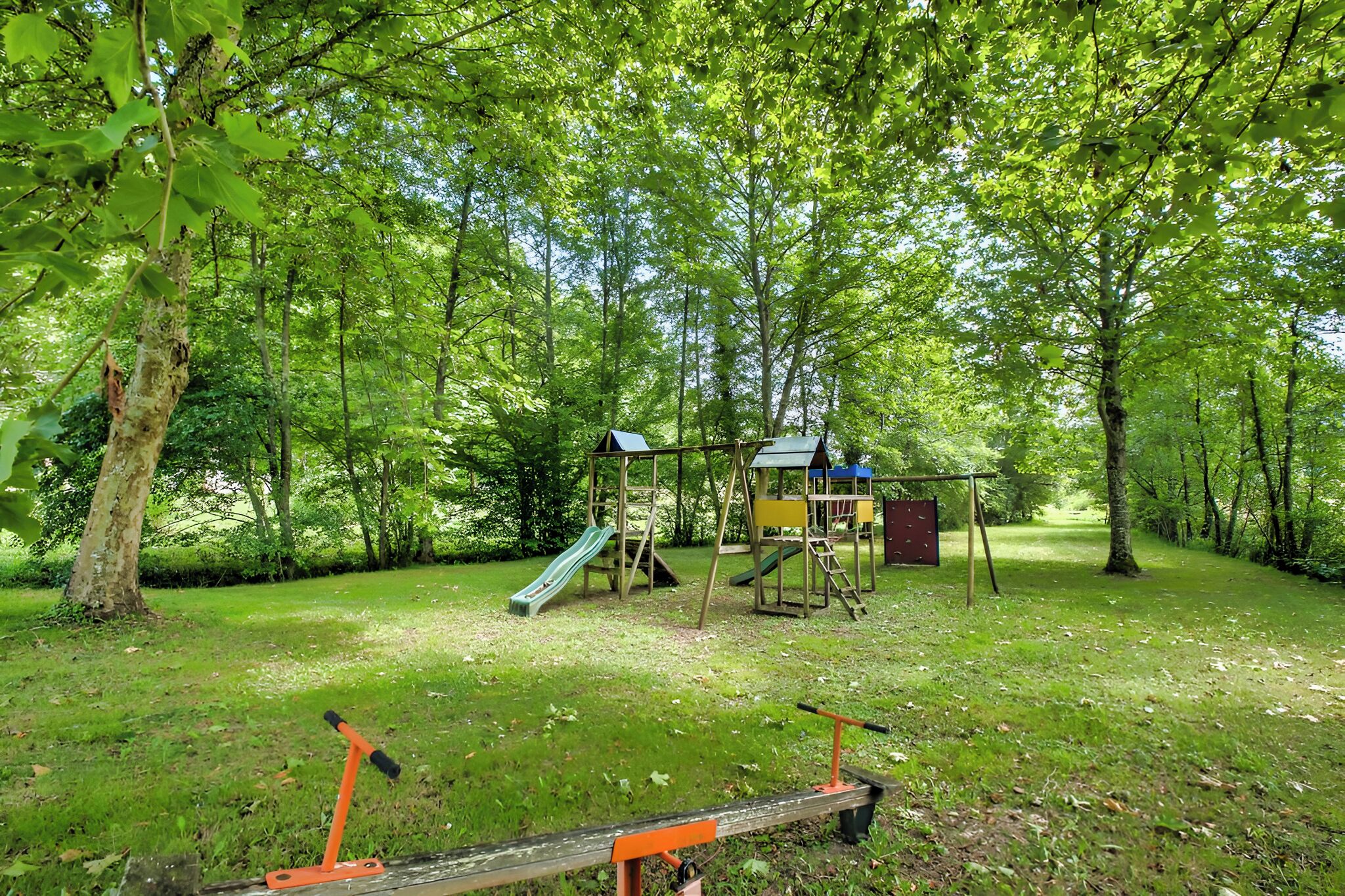Un terrain de jeux avec un toboggan et des structures d’escalade, le tout entouré d’arbres.