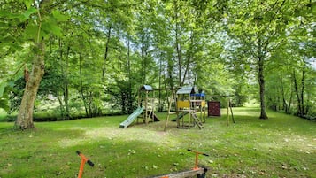 A playground with a slide and climbing structures surrounded by trees.