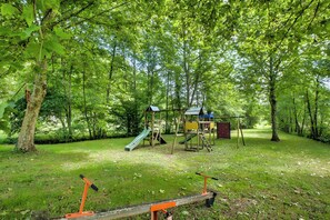 Un parque infantil con tobogán y estructuras para escalar, rodeado de árboles.