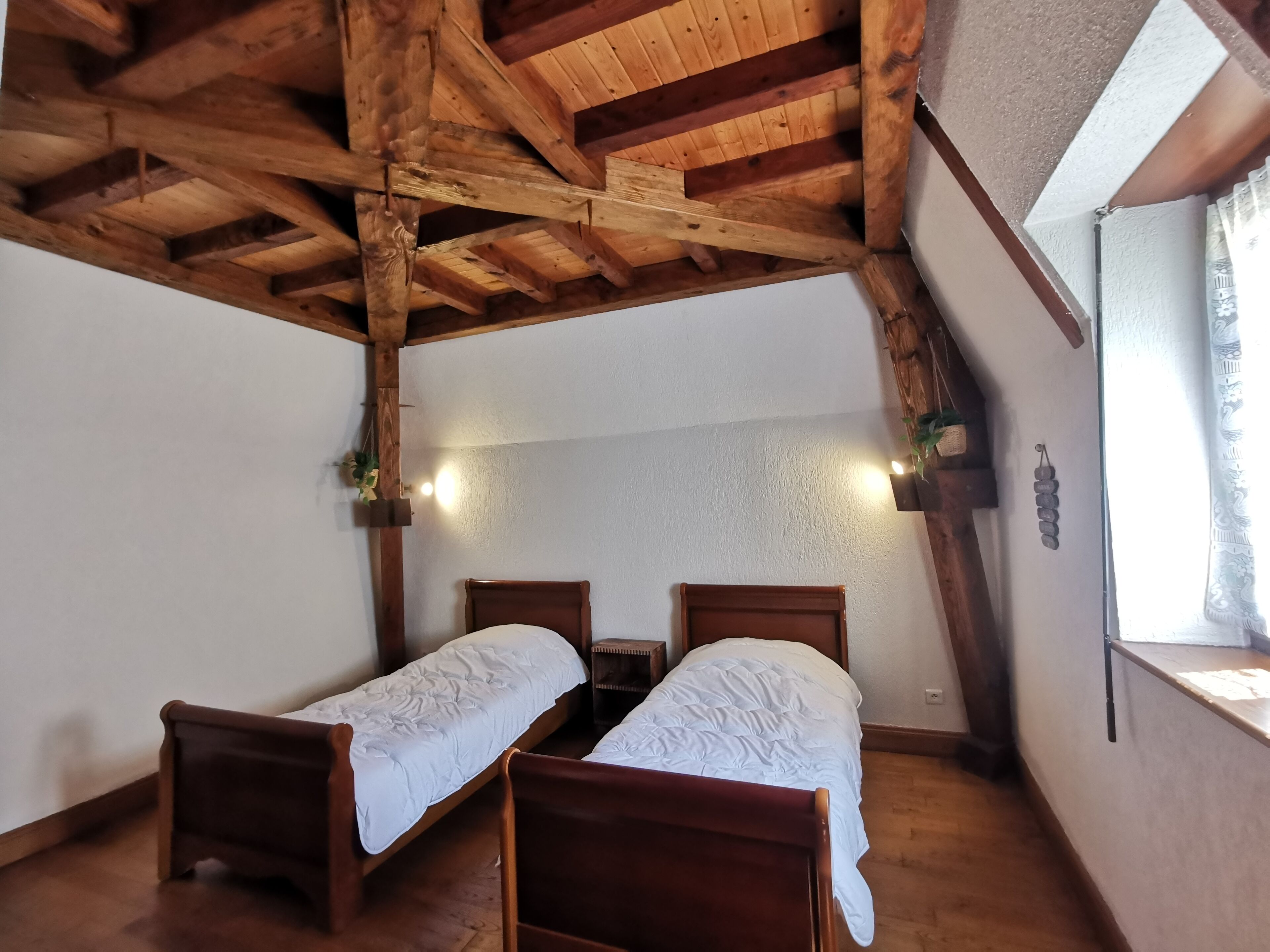 Ein Zimmer mit zwei Holzbetten, einer geneigten Decke und einem Fenster mit Vorhang.