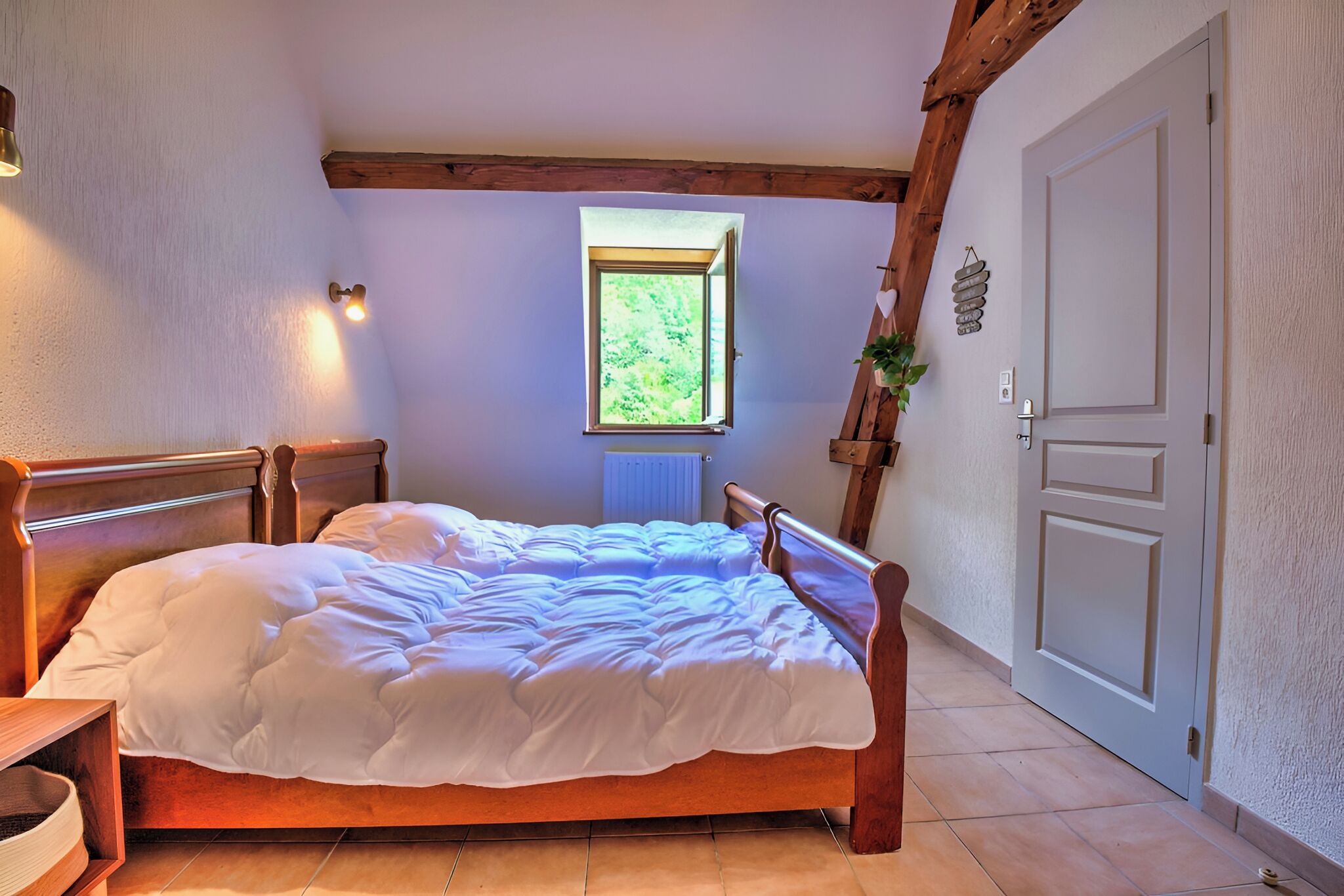 Un dormitorio con cama de madera, ventana con vista a follaje, radiador y puerta.