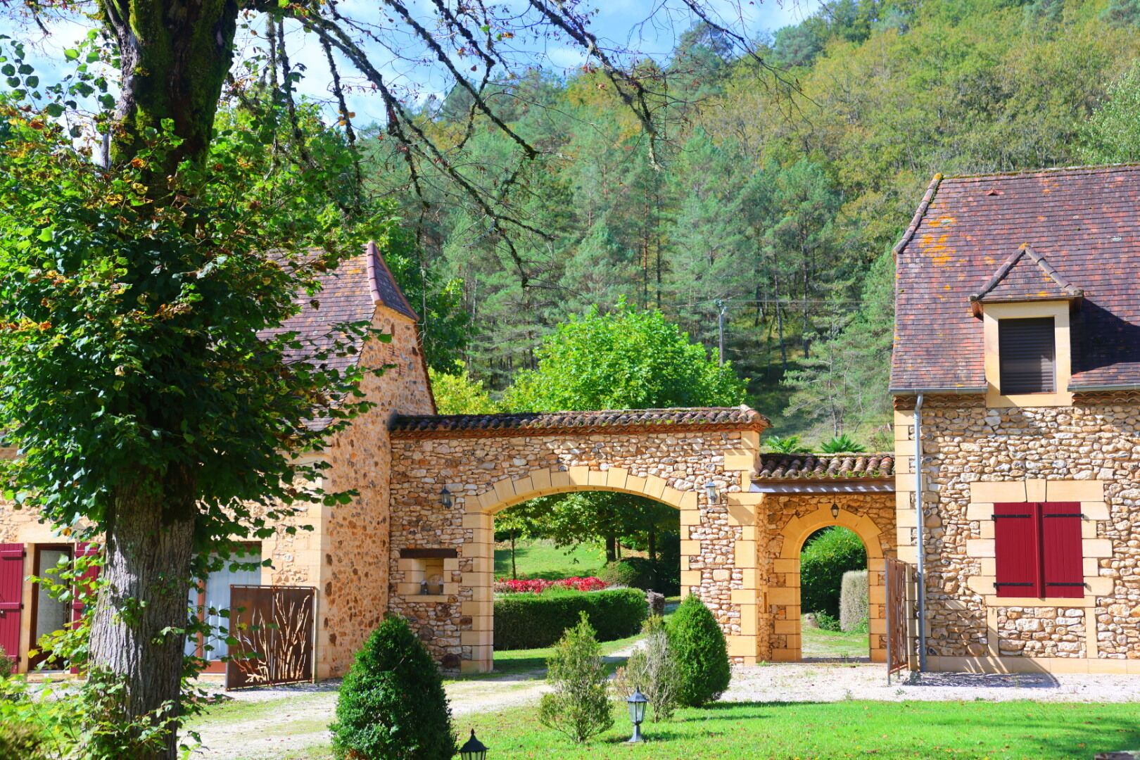 Um edifício de pedra com um arco de pedra, uma porta vermelha e um jardim bem cuidado.