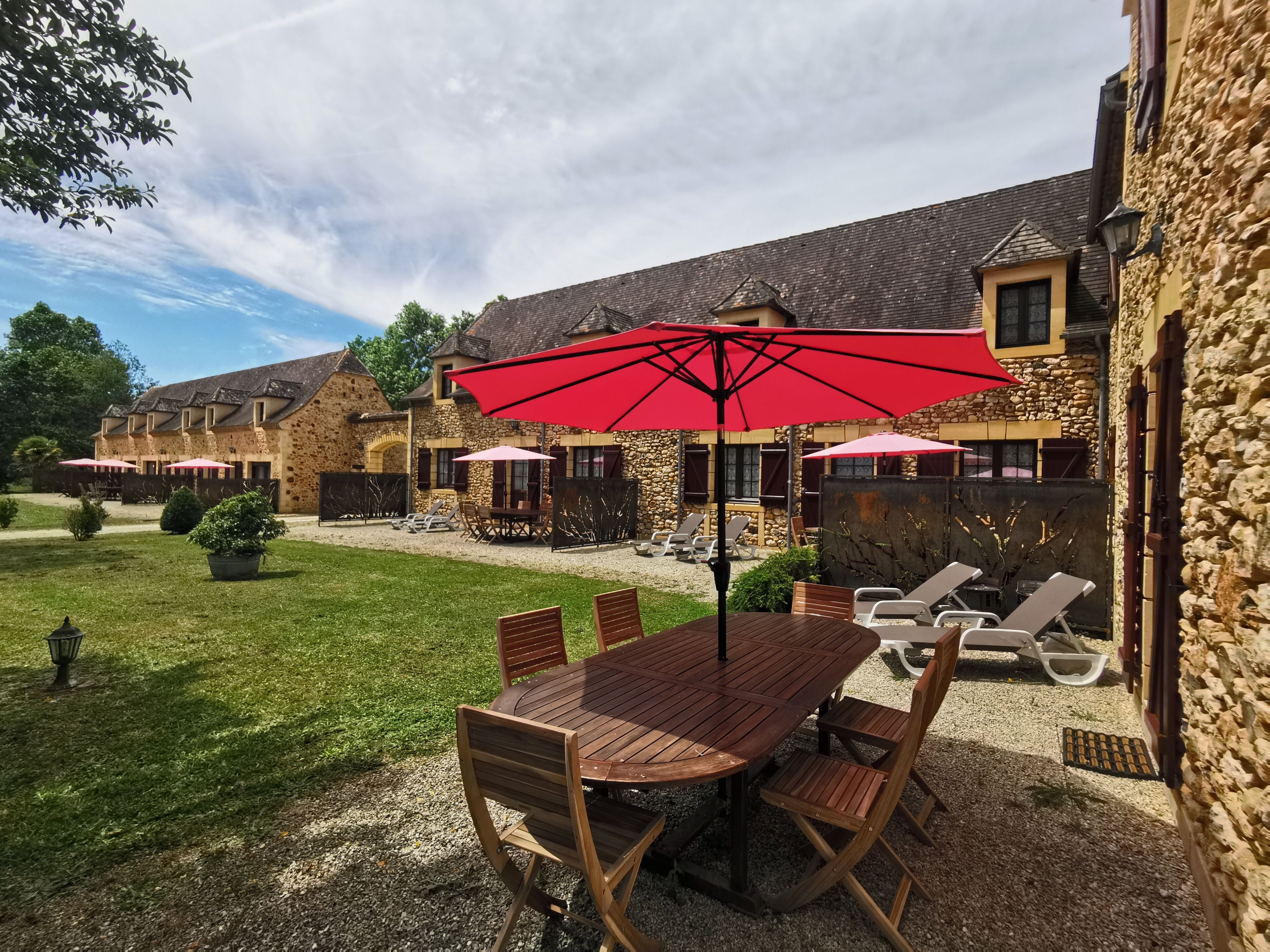 Eine Terrasse im Freien mit Holztisch und -stühlen, umgeben von Steinbauten und einer Kiesfläche.