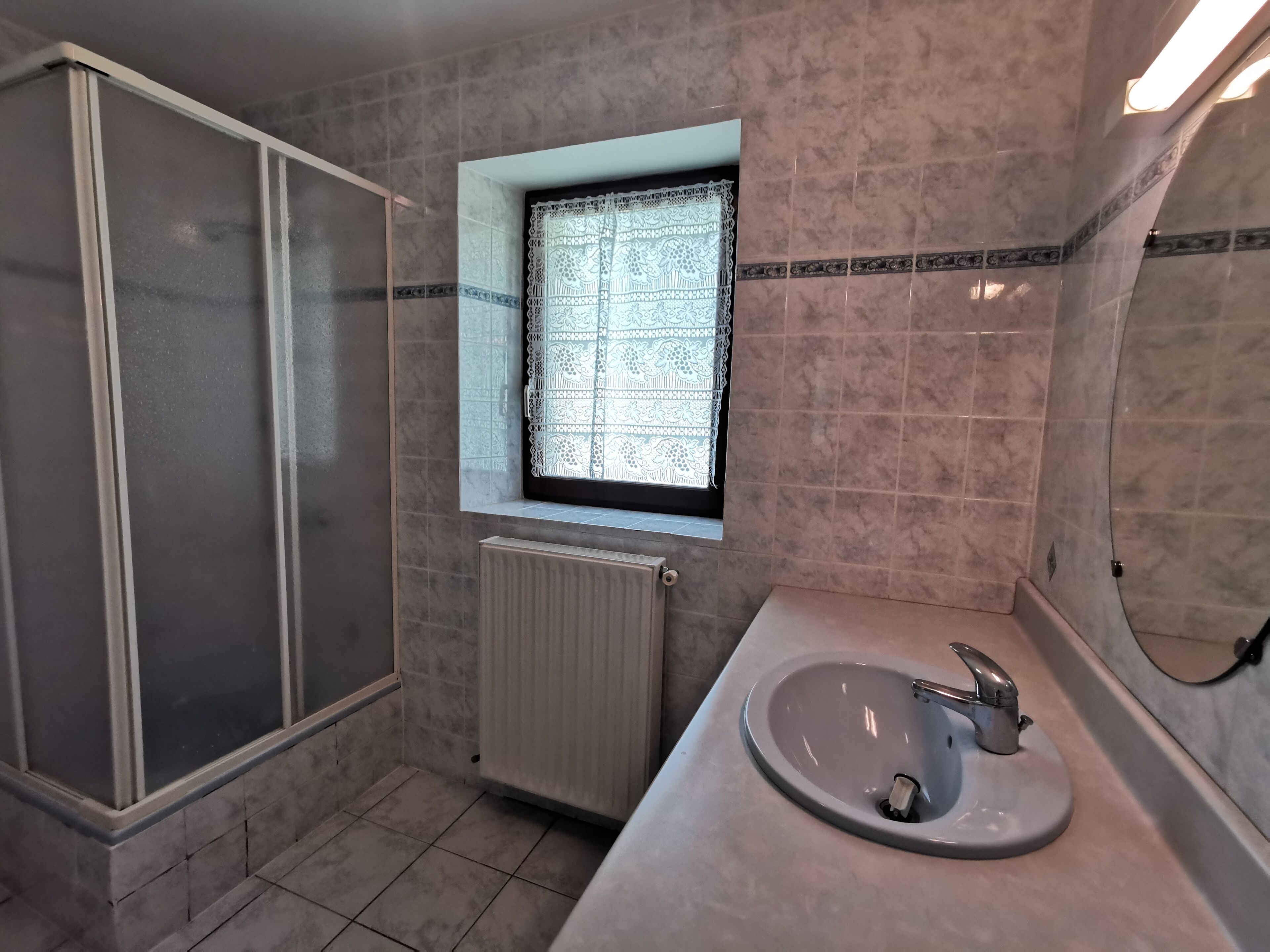 Un bagno con doccia, lavandino e finestra con tende a motivi decorativi.