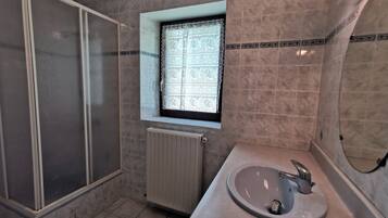 Un bagno con doccia, lavandino e finestra con tende a motivi decorativi.