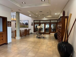 Eine Lobby mit einer Rezeption, einem Kaffee-Szcen, einem Essbereich mit Tisch und Stühlen sowie einer großen, schwarzen Vase.
