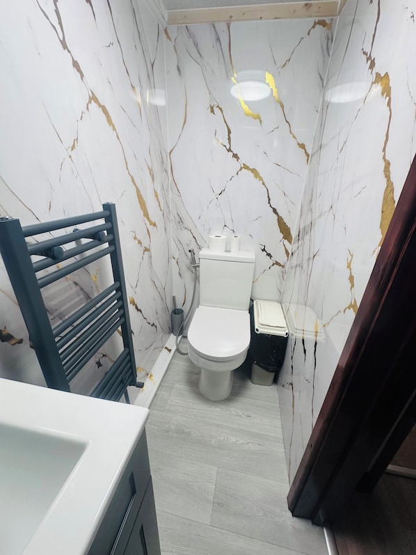 A bathroom with a toilet, a small trash bin, and a towel rack.