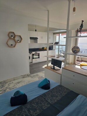 Ein modernes Zimmer mit Bett, Schreibtisch, Meerblick und einer Küchenzeile.