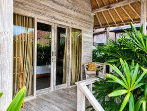 A wooden exterior with sliding glass doors, a wooden deck, and a thatched roof. - The Nicho’s Bungalows and Villas (Kabupaten Klungkung)