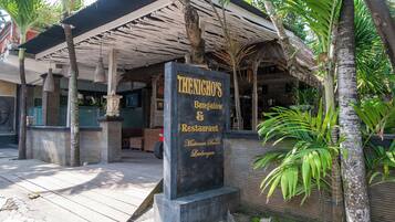 A sign for 'The Nicho's' restaurant with a covered outdoor seating area and tropical plants.