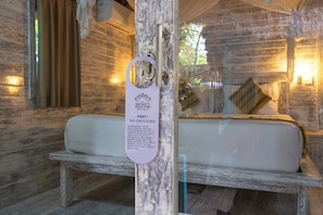 A rustic wooden room with a bed, a wooden bench, and a sign on the door. - The Nicho’s Bungalows and Villas (Kabupaten Klungkung)