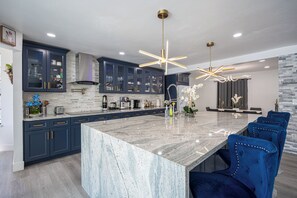 Een moderne keuken met donkere kastjes, een marmeren eiland en blauwe stoelen.