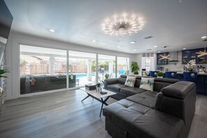 Een moderne woonkamer met een grote bank, een bijzettafeltje en uitzicht op een achtertuin met zwembad.