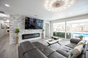 Een moderne woonkamer met een stenen muur, een flatscreen televisie, een open haard en een groot raam met uitzicht op een achtertuin.