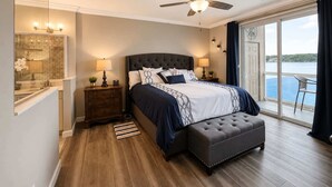 Une chambre à coucher comprenant un lit, un ventilateur de plafond, une table de chevet, un banc, une fenêtre avec vue et une porte.