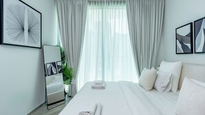 Una moderna camera d'hotel con un letto grande, lenzuola bianche, un comodino, uno specchio e una finestra con tende leggere.