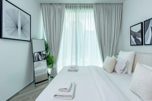 A modern hotel room with a large bed, white linens, a bedside table, a mirror, and a window with sheer curtains. - Urban-Luxury-reshaped Business District (Dubai)