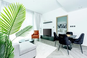 A modern living room with a sofa, a dining table with chairs, a TV, and a large window with curtains. - Urban-Luxury-reshaped Business District (Dubai)