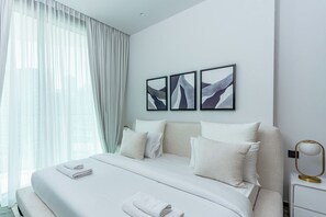 Ein modernes Hotelzimmer mit einem großen Bett, weißer Bettwäsche, einem Nachttisch mit Lampe und abstrakter Wandkunst.
