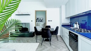Una cucina moderna con mobili bianchi, un piano di lavoro blu e un'area pranzo con sedie nere e un tappeto bianco.