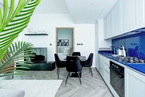 A modern kitchen with white cabinets, a blue countertop, and a dining area with black chairs and a white rug. - Urban-Luxury-reshaped Business District (Dubai)