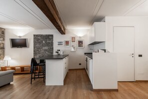 A compact kitchen with a central island, a built-in stove, and a flat-screen TV mounted on the wall. - Nucia Studio in the heart of Como (Como)