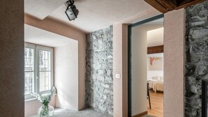 Una habitación con pared de piedra, techo de madera, ventana con persianas y puerta que da a otra estancia.