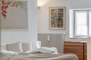 A bedroom with a bed, a radiator, a window, and a framed abstract painting on the wall. - Nucia Studio in the heart of Como (Como)
