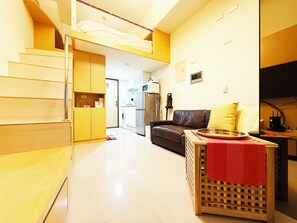 En kompakt opholdsstue med tekøkken, sofa, spiseplads og trappe til en etage ovenover.