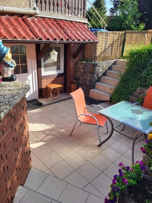 A patio area with a table and chairs, a brick wall, a stone staircase, and a small garden with flowers. - Vacation apartment Zwergenstübchen (Lübstorf)