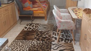 Una cama litera infantil con escritorio y silla, un microondas y una alfombra estampada en una habitación pequeña.