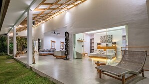 Interior moderno de hotel com sala de estar ampla, área de jantar e quarto com cama grande e mesas de cabeceira.