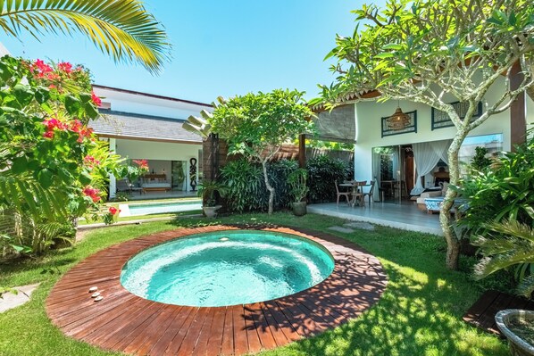 Un jardin avec une piscine, une terrasse en bois et un espace patio aménagé avec du mobilier d’extérieur.