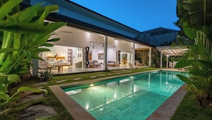 Uma casa moderna com piscina, área de estar externa e plantas tropicais.