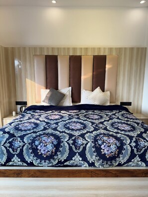 Uma cama com colcha estampada, cabeceira com painéis verticais e abajures laterais.