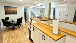 Cozinha moderna com bancada de madeira, armários brancos e área de jantar com mesa e cadeiras.