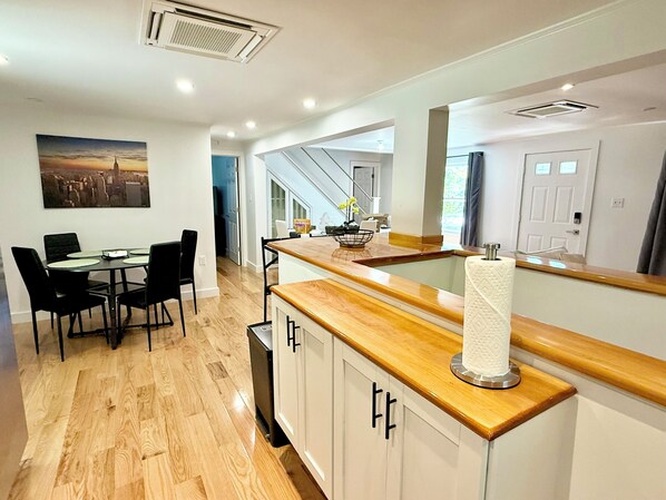 A modern kitchen with a wooden countertop, white cabinets, and a dining area with a table and chairs.