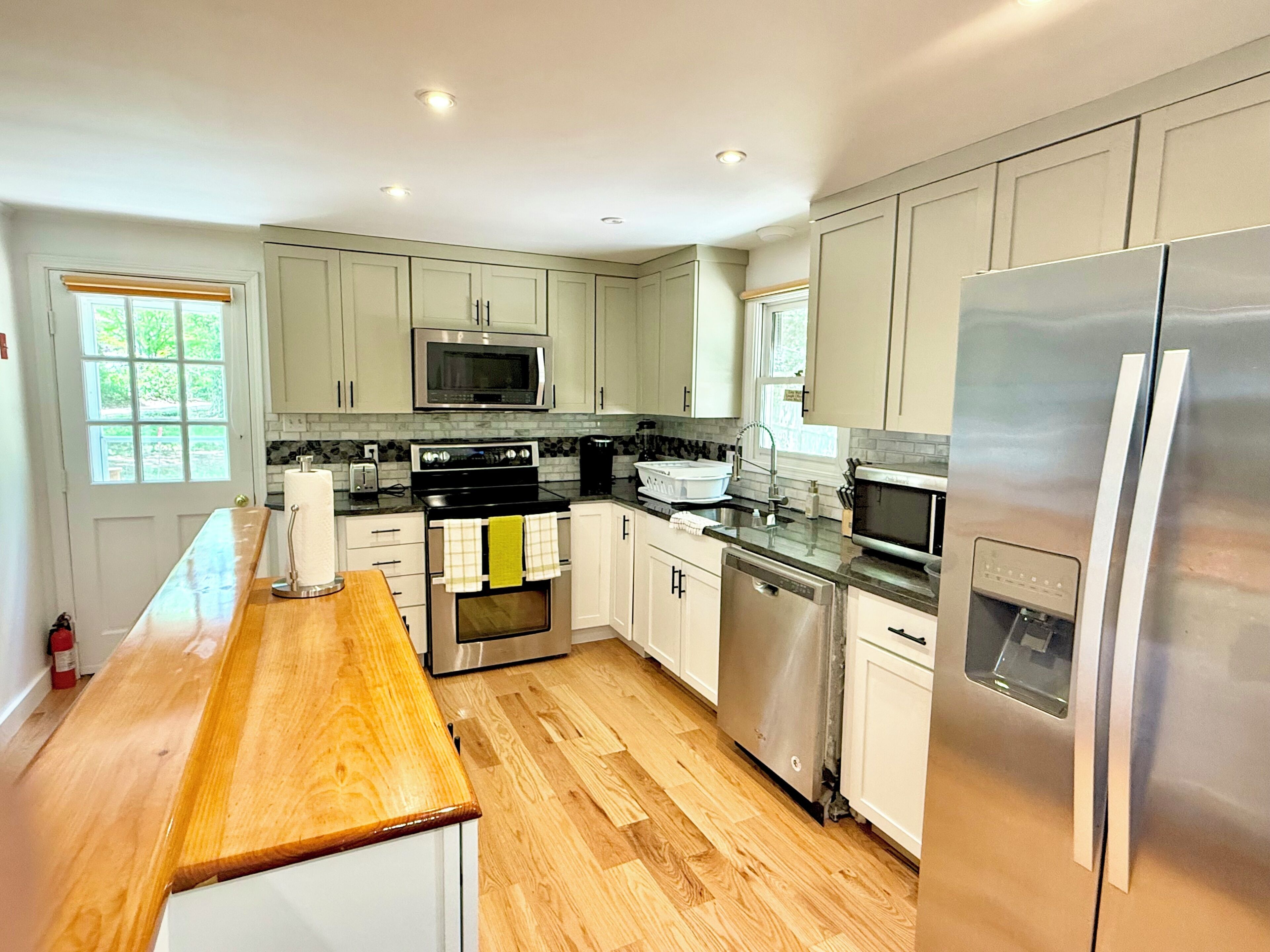 A modern kitchen with stainless steel appliances, wooden countertops, and light-colored cabinetry.