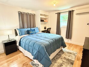 A bedroom with a bed, a nightstand, a desk, and a window with curtains. - Spacious 3-bedroom building in peaceful Tisbury with AC (Tisbury)