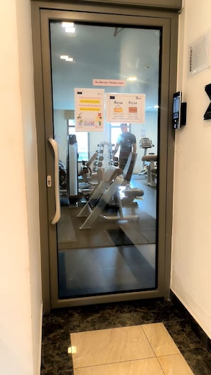Ein Fitnessraum mit Trainingsgeräten, einer Glastür und einem digitalen Bildschirm.