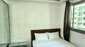 Una camera d'albergo con un letto, un comodino, uno specchio e una finestra vista edifici.