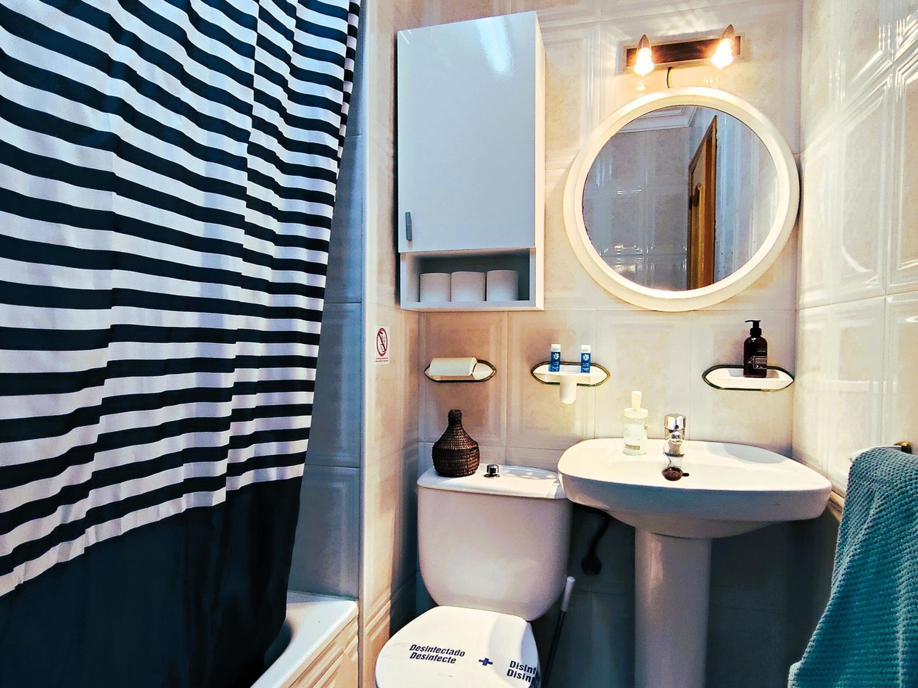 A bathroom with a striped shower curtain, a toilet, a sink with a mirror, and a soap dispenser.