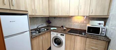 A compact kitchen with a washing machine, a microwave, and a refrigerator.