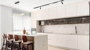 Eine moderne Küche mit Marmorarbeitsplatte, weißen Schränken und einer Bar mit Sitzgelegenheiten.