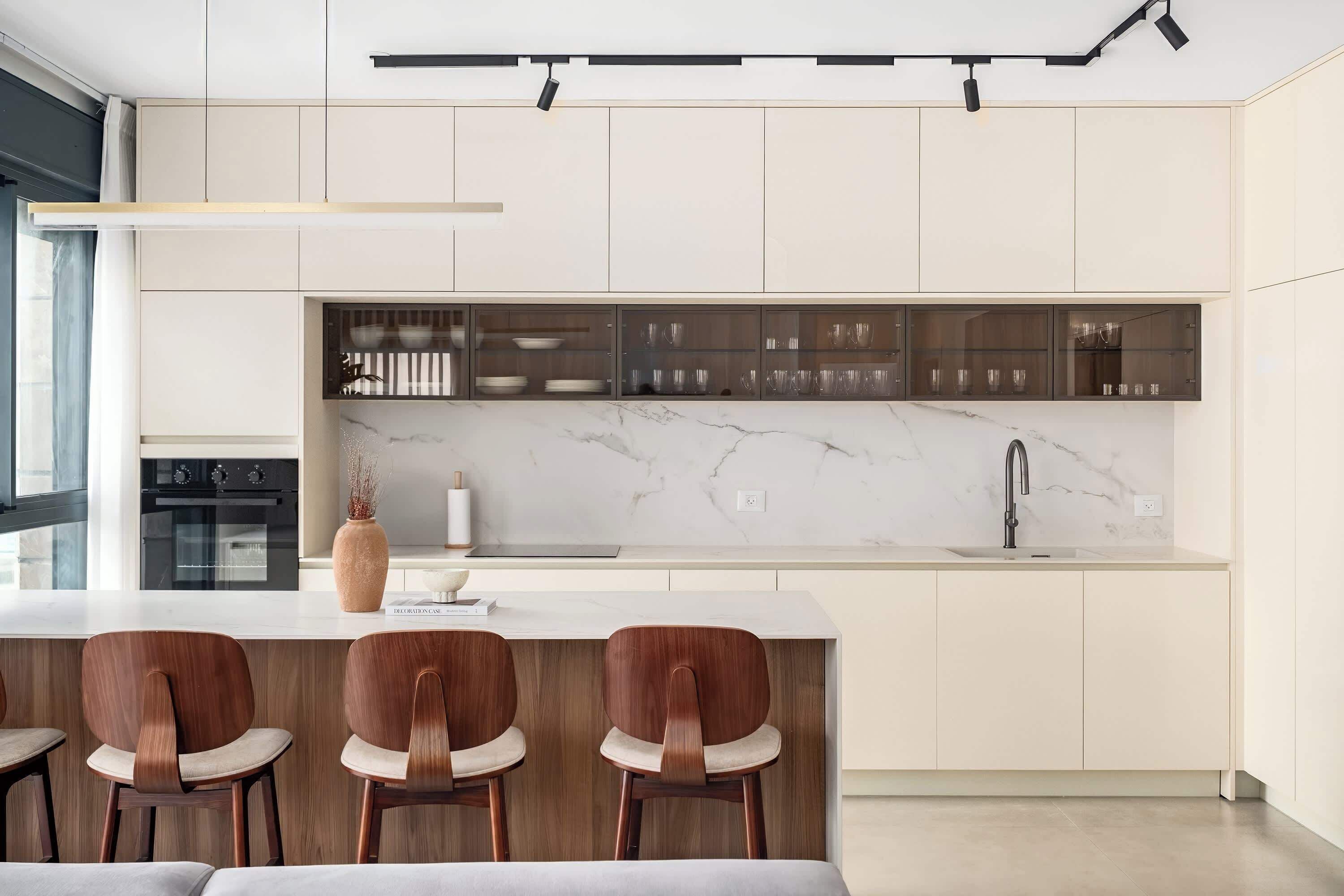 Une cuisine moderne dotée d’un plan de travail en marbre, de meubles de rangement intégrés et d’un coin bar avec des tabourets.