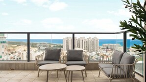 Ein Balkon mit zwei Stühlen und einem Tisch, der auf eine Stadtansicht und das Meer blickt.